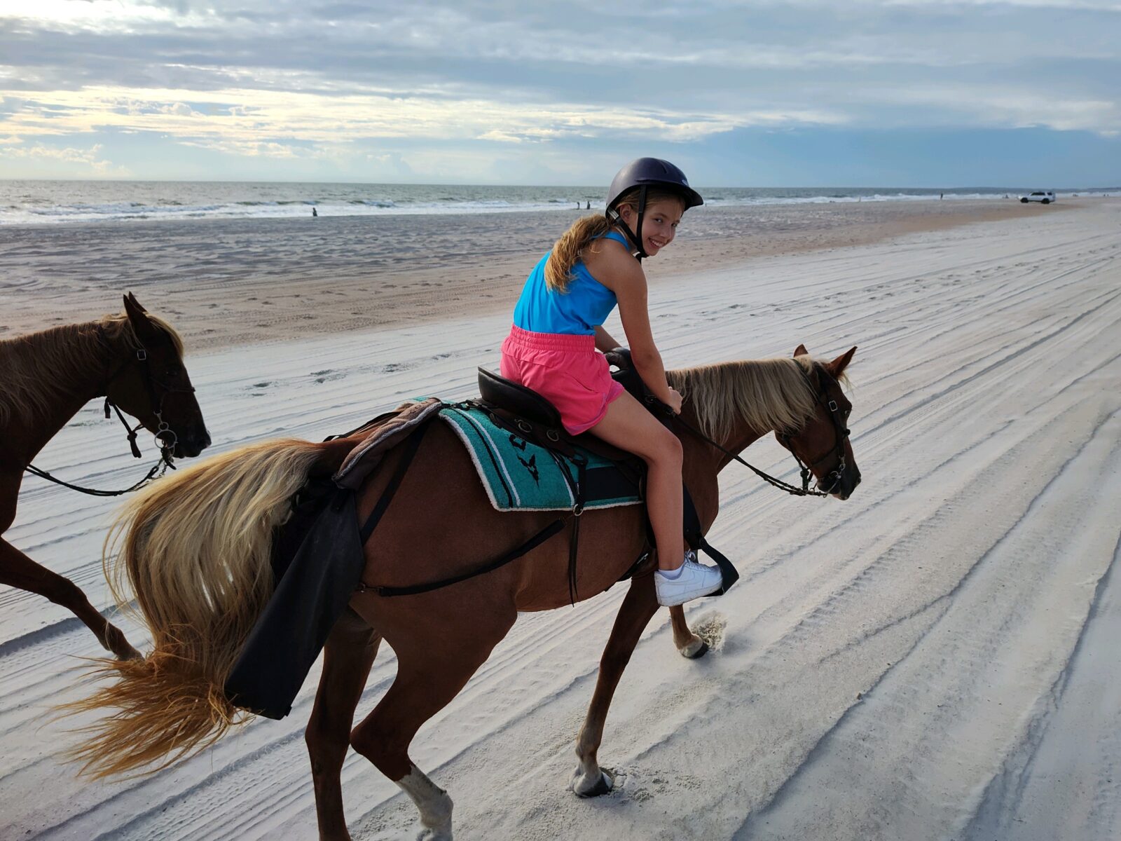 Girl in helmet riding a horse on a beach with ocean in background.