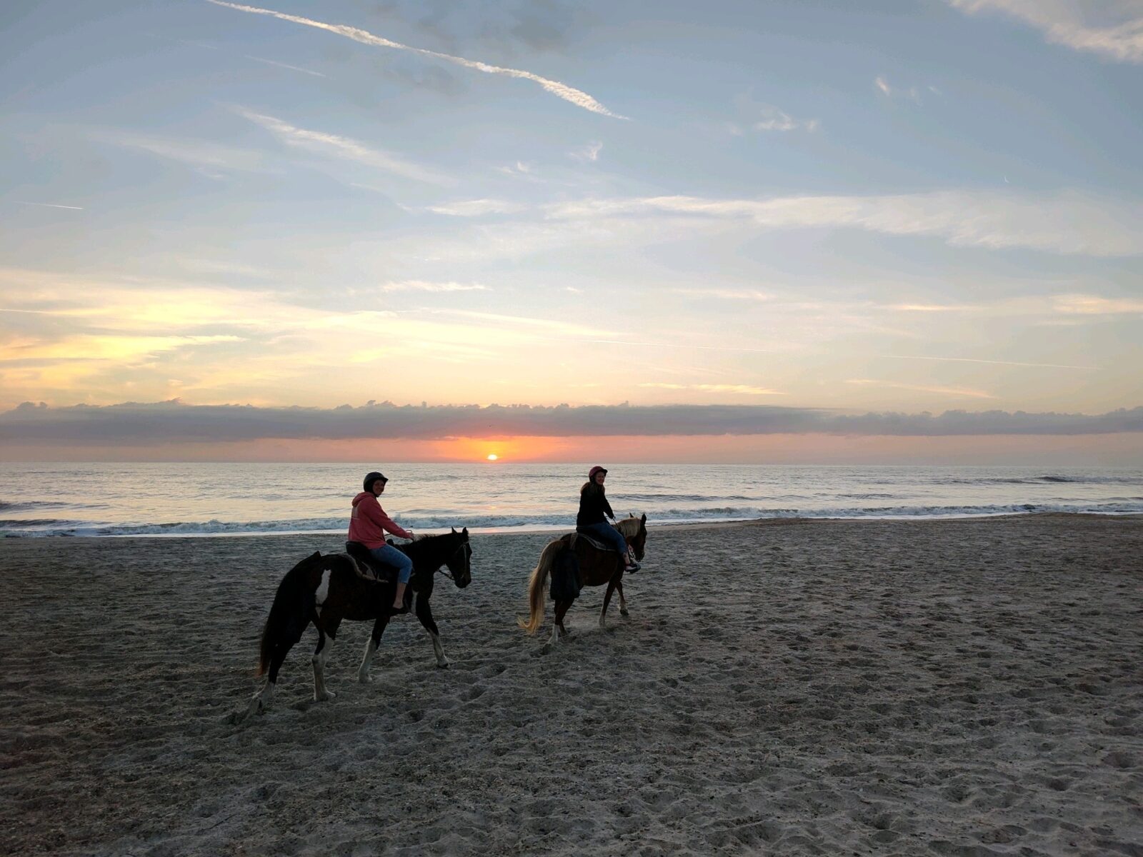 Two people riding horses on a beach at sunset.