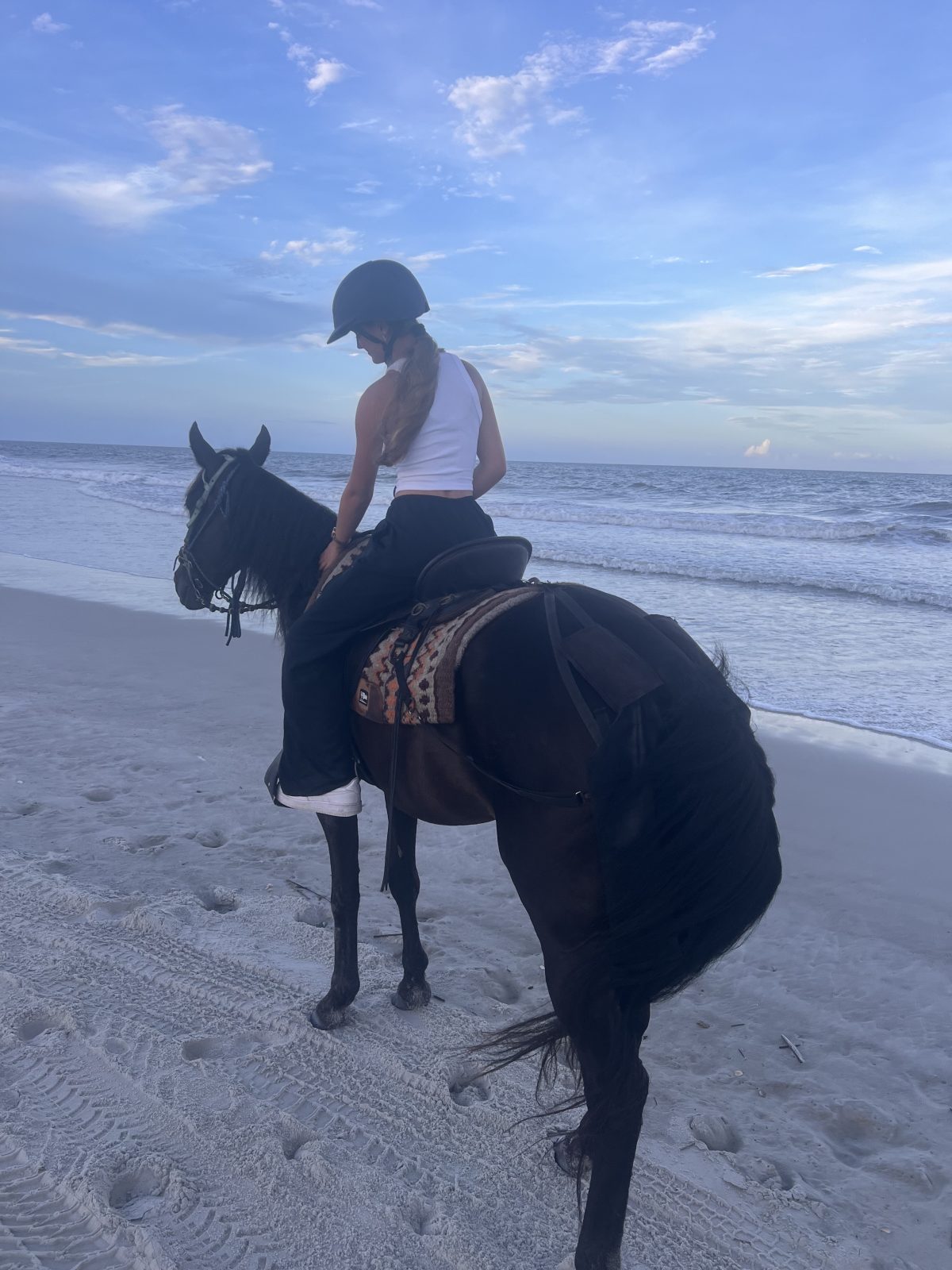 Person riding a horse on the beach under a blue sky.