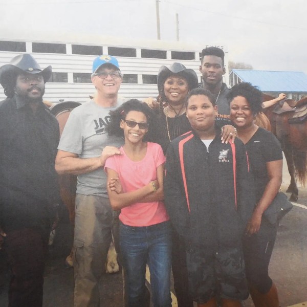 Group of seven people smiling in front of horses and a trailer.