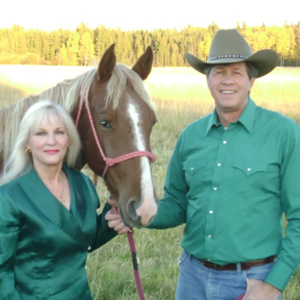 Couple in green shirts with a brown horse in a field.