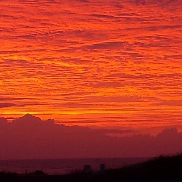 Vivid orange and pink sunset with silhouette of a pavilion and person on a hill.